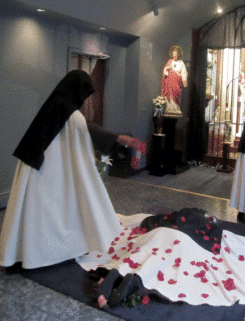 The youngest Sister sprinkles rose petals on the newly professed who is lying prostrate on the cross of flowers.